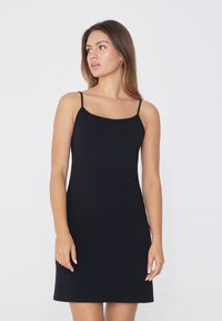 Černé šaty bez rukávů s tenkými ramínky, rovně ustřiženým výstřihem a přiléhavým střihem. Hladká tkanina a délka po kolena.