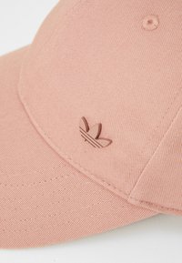 Pink cap made of textured fabric, featuring a small embossed logo with three leaves. The design includes a curved brim and stitched details.