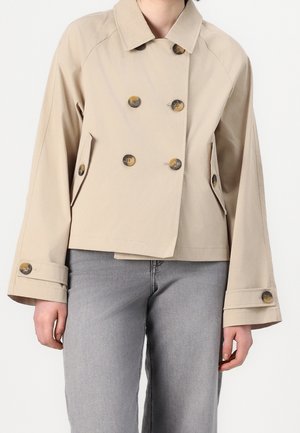 Veste courte beige à double boutonnage avec de grands boutons et des poches à rabat, portée avec un jean gris clair.