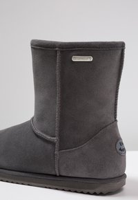 Stivale alla caviglia impermeabile grigio realizzato in morbida pelle scamosciata. Presenta una superficie liscia, cuciture rinforzate e una suola piatta in gomma con dettagli del logo.