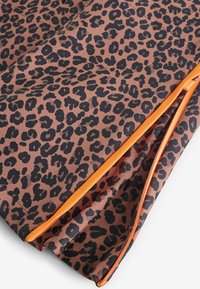 Brązowa tkanina w wzór cętek lamparta z czarnymi plamami. Posiada jaskrawo pomarańczowy zamek błyskawiczny i gładką teksturę. Zakrzywiony kształt z widocznymi szwami.