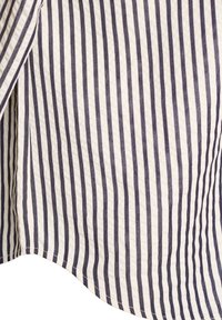 Valge kangas, millel on vertikaalsed mustad triibud, lähedalt vaadatuna särgi kaarduva hem'i ja osa varruka kohta.