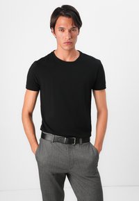 Svart kortärmad T-shirt av mjukt tyg, kombinerad med gråmönstrade byxor och ett svart läderbälte med en silverspänne.