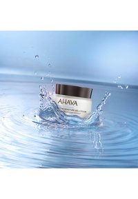 AHAVA Active Moisture Gel Cream i en vit burk med ett mörkbrunt lock, omgiven av vattendroppar och ringar på en blå bakgrund.
