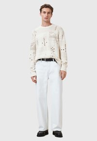 Knit cream sweater with open patterns and dotted details, paired with light-colored, straight-leg trousers, and black shoes.