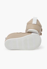 Sneaker alta beige con superficie testurizzata, suola bianca e dettagli con strap in velcro. Suola in gomma con scanalature verticali per una migliore aderenza.
