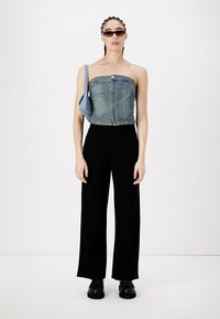 Denim beznaramenasti top, crne hlače širokih nogavica, crne platforme i mala plava torba. Model nosi smeđe sunčane naočale i ima pletenu kosu.