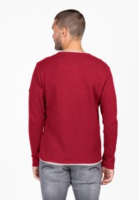 Chemise à manches longues en tricot de gaufre rouge avec un col rond, des poignets côtelés et un ourlet droit, associée à un jean gris clair.