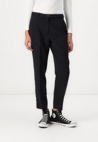 Pantalons noirs ajustés avec une coupe slim, présentant une taille avec passants de ceinture et une texture lisse, associés à des baskets montantes noires.