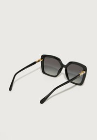 Occhiali da sole neri oversize con montatura quadrata, lenti scure sfumate, accessori in oro alle cerniere e aste nere lucide. Presenti dettagli testurizzati.