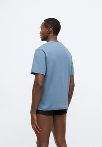 Kék texturált, kerek nyakú póló rövid ujjakkal, laza szabással és finom bordázott mintával.