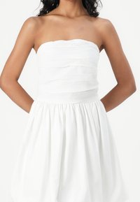 Bílé šaty bez ramínek s texturovaným živůtkem a nařasenou sukní. Vyrobené z lehké látky s hladkým povrchem a elastickým pasem.
