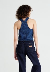 Top corto in denim con design a incrocio sul retro, caratterizzato da un motivo testurizzato. Abbinato a jeans in denim scuro a vita alta con dettagli visibili sulle tasche posteriori.