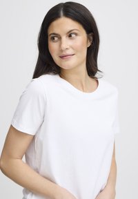 Balti medvilniniai marškinėliai trumpomis rankovėmis su apvalia iškirpte, laisvo silueto ir lygaus paviršiaus.