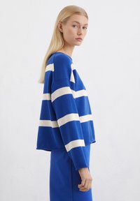 Blau gestreifter Pullover mit weißen horizontalen Streifen, oversized Schnitt, gerippter Kragen und Bündchen, kombiniert mit einem passenden blauen Rock.