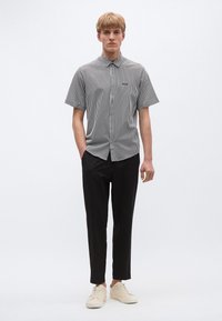 Cămașă cu mâneci scurte în dungi alb-negru, cu nasturi frontali, combinată cu pantaloni negri conici și adidași crem. Design simplu și modern.