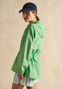 Zaļa viegla kapuce ar auklu vidukli un elastīgām aprocēm. Iekļauj baltu apmale un sānu kabatas. Apvienota ar svītrainām šortiem.