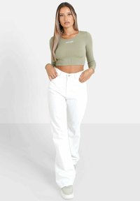 Olivgrön ribbad cropped tröja med långa ärmar och vita högmidjade byxor. Modellen bär grå sneakers och visar upp en avslappnad outfit.