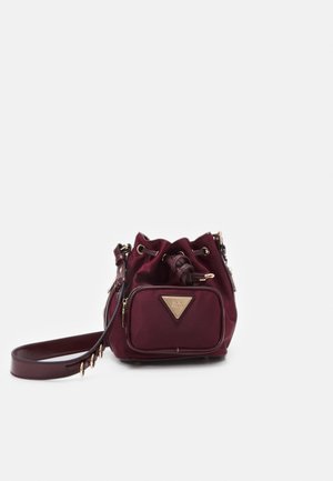 Kleine burgunderrote Beuteltasche mit Kordelzug, Vorderreißverschlusstasche und verstellbarem Schulterriemen vor weißem Hintergrund.