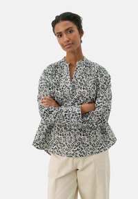 Blusa nera e bianca con motivo floreale, colletto rotondo, maniche lunghe a sbuffo e una linea vita che si allarga dolcemente.
