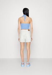 Haut halter en crochet bleu clair associé à un short brodé blanc, avec un patch en cuir tan. Des sandales à plateforme bleues complètent le look.