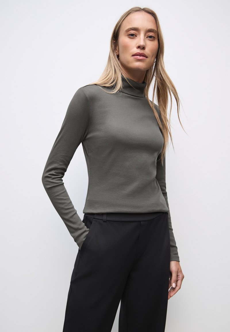 Collo verde fitted a maniche lunghe con collo alto, realizzato in tessuto a coste, abbinato a pantaloni neri. La parte superiore presenta una superficie liscia e una silhouette aderente.