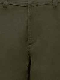Gros plan sur le tissu d’un pantalon vert olive montrant la ceinture, les passants de ceinture et la couture de la fermeture éclair avant.