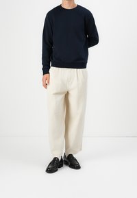 Marinblå sweatshirt med rund halsringning, kombinerad med cremefärgade byxor med vida ben. Svarta loafers med slät textur och subtila detaljer.