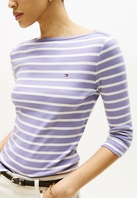 Gestreiftes Langarmshirt in Helllila und Weiß, mit einem Bootsausschnitt und einem kleinen Logo auf der Brust. Weicher Stoff mit enganliegendem Schnitt.