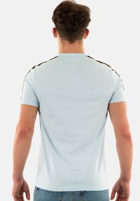 Camiseta de manga corta azul claro con un diseño sencillo, que presenta acentos negros en los hombros y una textura suave y lisa.