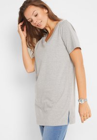 T-shirt grigio a maniche corte con scollatura a V e fessure laterali, realizzato in tessuto morbido. Abbinato a un orologio grigio, indossato con jeans blu.