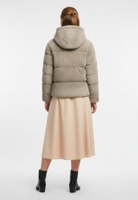Kurtka puchowa w prążkowanej beżowej tkaninie z kapturem, zestawiona z jasnoróżową, zwiewną spódnicą i czarnymi botkami za kostkę.
