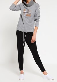 Grijze sweatstof met capuchon en een motief op de voorkant. Gecombineerd met zwarte taps toelopende broek en witte instapschoenen.