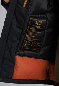 Črna puhovka z oranžno podlogo, opremljena z oznako za nego, žepom na zadrgo in nastavljivim pokrovom s vrvico.