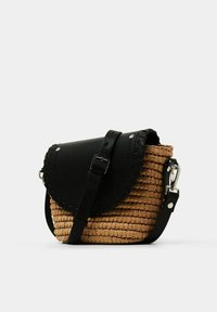 Tkaná slaměná crossbody taška s černou koženou klopou a popruhem, s hladkým povrchem a stříbrnými kovovými akcenty.