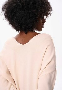 Lange mouwen, lichtbeige gebreide trui met een brede V-hals en een schouderlijn die is verlaagd. Getextureerde stof met een gladde afwerking aan de achterkant.