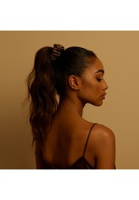 Brązowa satynowa gumka do włosów trzymana w wysokim kucyku; teksturowane falowane włosy, widok z boku sylwetki na tle stonowanego beżowego tła.