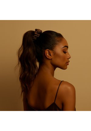 Brązowa satynowa gumka do włosów trzymana w wysokim kucyku; teksturowane falowane włosy, widok z boku sylwetki na tle stonowanego beżowego tła.