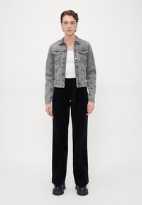 Gray denim jacket with front pockets, worn over a white tank top. Black corduroy high-waisted pants, featuring a tie detail at the waist.