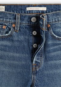 Jeans de mezclilla azul con cierre de botón, remaches de cobre, costuras naranjas y etiquetas que dicen "WEDGIE STRAIGHT" y "PREMIUM."