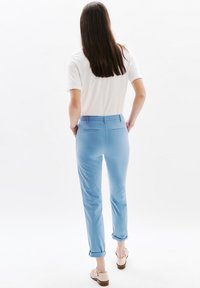 Lichtblauwe katoenen broeken met opgerolde pijpen en standaard achterzakken, gecombineerd met een witte top met korte mouwen. Model staat met de rug naar de kijker, waardoor de achterkant zichtbaar is.