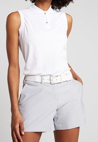 Polo blanc à manches courtes avec col et deux boutons, associé à un short gris clair et une ceinture blanche texturée. Tissu lisse et coupe ajustée.