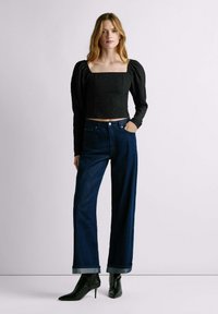 Top corto nero con maniche a sbuffo, tessuto testurizzato; abbinato a jeans a gamba larga blu scuro con orlo arrotolato e stivali neri a punta.