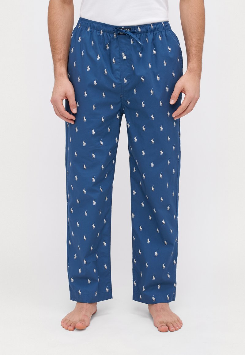 Pantalons de pyjama bleus présentant un motif de logo blanc répétitif, une taille élastique avec cordon de serrage, et un design décontracté à jambe droite.