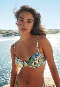 Cvetlični bikini z živahnimi modrimi, rumenimi in zelenimi vzorci. Material je videti gladek, z nastavljivimi naramnicami in nabranim dizajnom na skodelicah.
