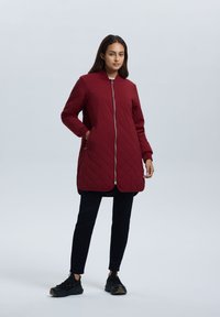 Bordeaux geborduurd jack met hoge kraag, volledige ritssluiting en zijzakken. Gecombineerd met zwarte broek en zwarte sneakers.