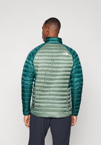 Gewatteerde jas in groene tinten met een hoge kraag, contrasterende mouwen en een gestikt ontwerp. Logo weergegeven op de achterkant van de schouder.