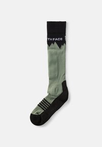 Calcetín hasta la rodilla en verde claro con un puño negro que presenta un estampado de montaña y un logo blanco. Las áreas de los dedos y el talón son negras con acentos a rayas.