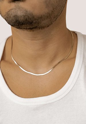 Thin, two-tone necklace featuring smooth silver and gold metal with a subtle wave design, worn on a bare neck above a white shirt.