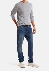 Grå långärmad tröja, blå denimjeans med blekningar, svart bälte, vita sneakers med bruna sålar. Fokusera på avslappnad, modern passform och design.